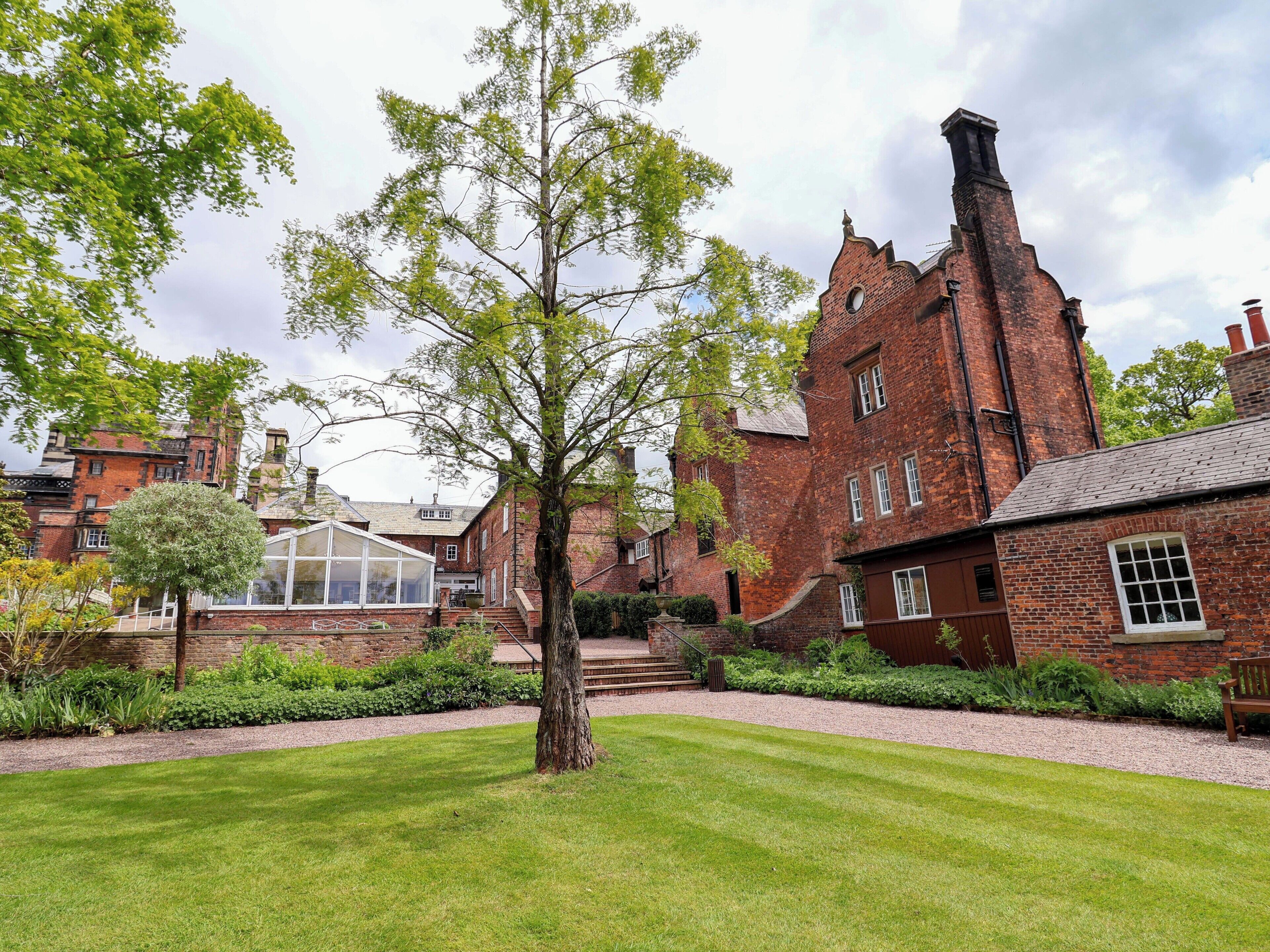 A traditional brick building with a large tree in the foreground, a conservatory, and a well-maintained lawn.