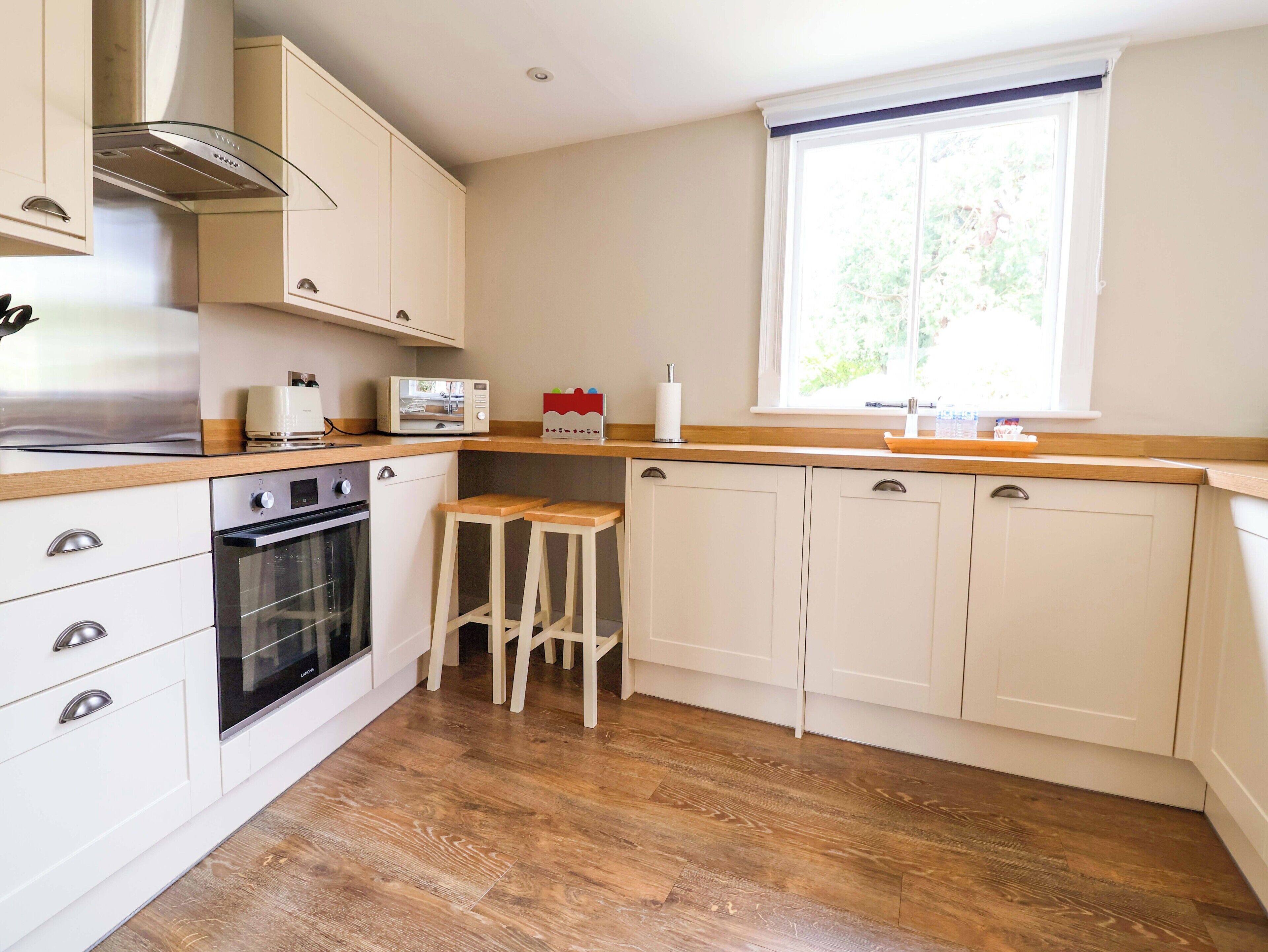 A kitchen with a microwave, oven, wooden stools, and a window.