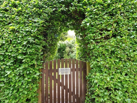 A wooden gate with a sign reading 'SOUTH TOWER' surrounded by dense green foliage.. South Tower Cottage