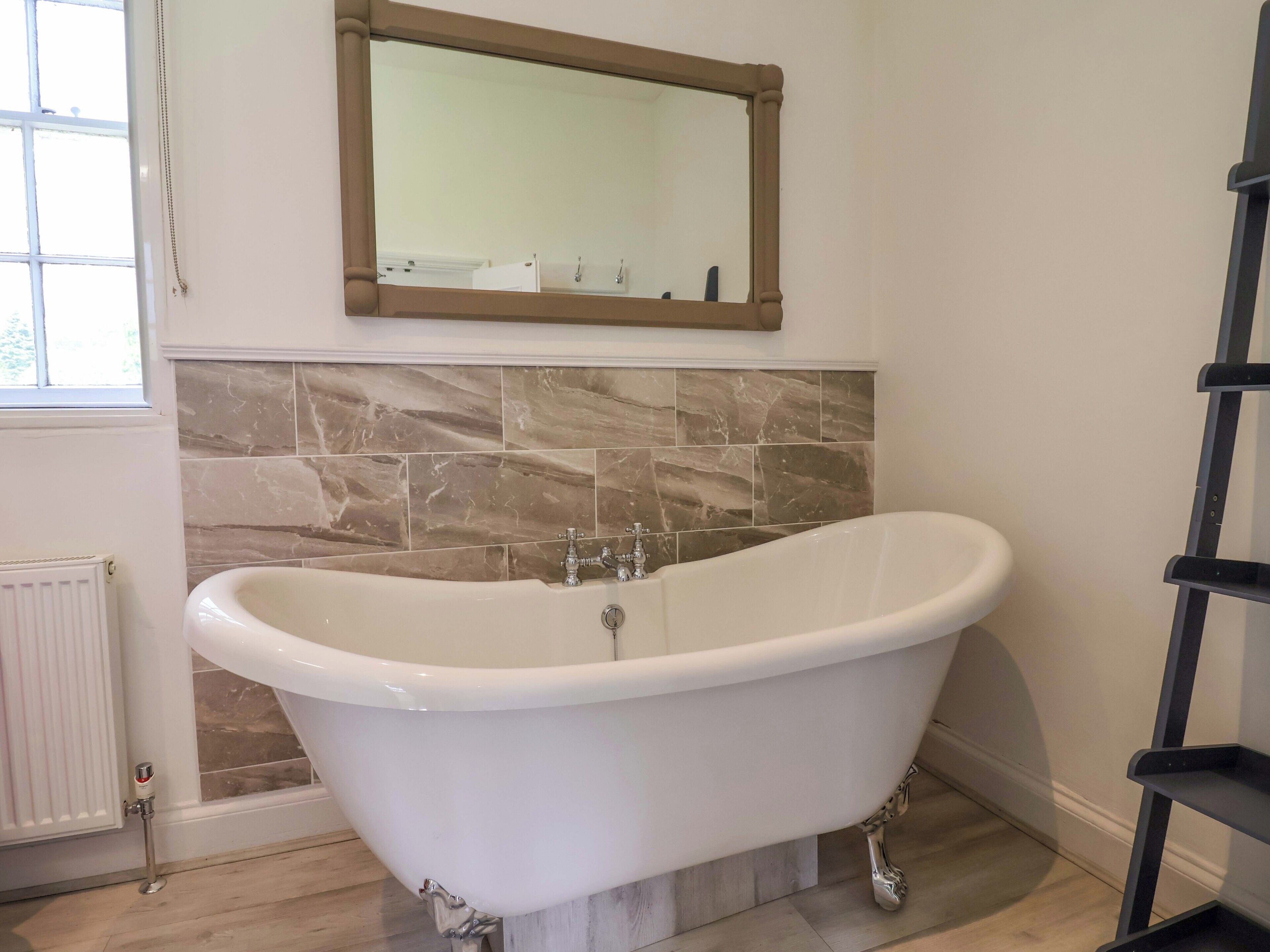 Un bagno con una vasca freestanding, uno specchio sopra e un termosifone a sinistra.
