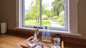 Una ventana con vista a un jardín, una bandeja con un recipiente con forma de corazón, dos botellas de agua y una caja de galletas de chocolate.