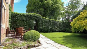 Un jardín con un sendero de piedra, un seto bien cuidado y un banco de madera.
