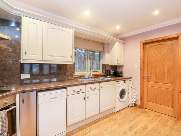 Una cocina compacta con armarios blancos, lavavajillas integrado, lavadora y puerta de madera.