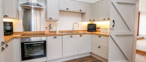 A modern kitchen with white cabinetry, a built-in oven, a microwave, and a stainless steel range hood.