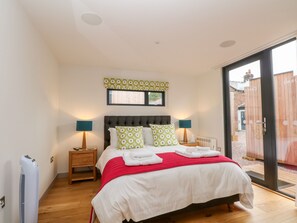 A bedroom with a bed, two bedside tables with lamps, a radiator, and a window with blinds.