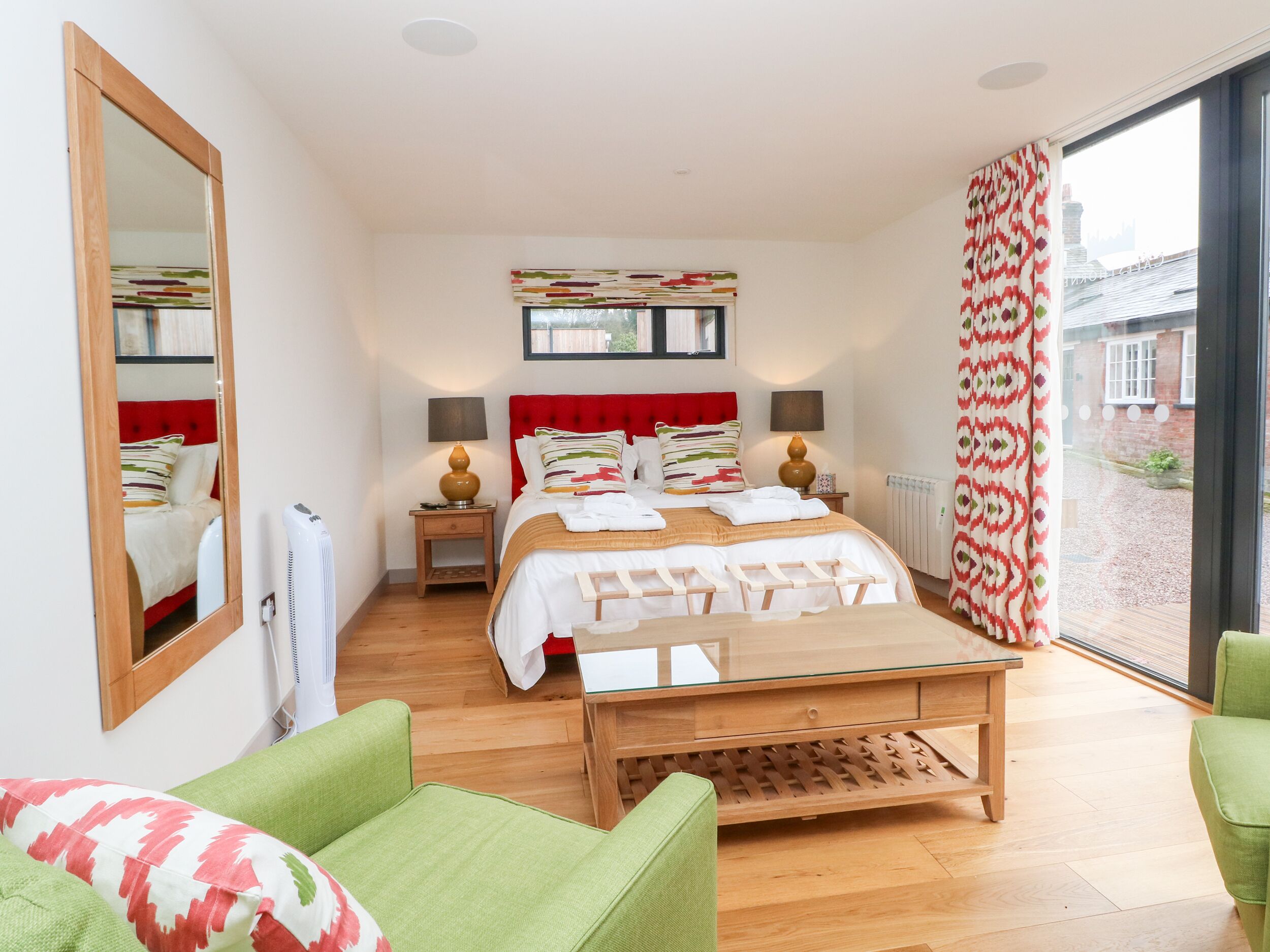 A bedroom with a bed, bedside tables, a mirror, a window with curtains, and a view of the outside.