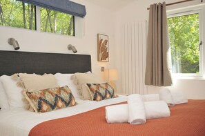 A hotel room with a bed, pillows, a lamp, a window with curtains, and a view of trees. - The Hideout (Looe)