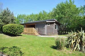 A small wooden cabin with a porch, surrounded by greenery and trees. - The Hideout (Looe)