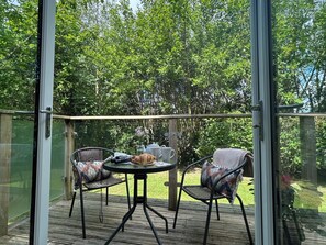 A covered outdoor patio with a table and chairs, surrounded by greenery. - The Hideout (Looe)