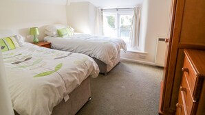 A bedroom with two beds, a window with curtains, and a wooden wardrobe. - 3 Rose Cottages (Looe)