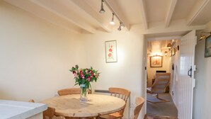 A dining area with a round wooden table, six wooden chairs, a vase with flowers, and a painting on the wall. - 3 Rose Cottages (Looe)