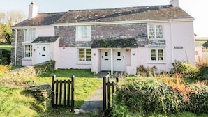 A pink cottage with a brick facade, numbered doors, and a small garden with a wooden gate. - 3 Rose Cottages (Looe)