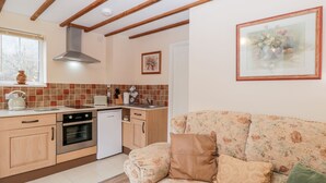A kitchen with wooden cabinets, a dishwasher, and a stove. There is a window with a view of trees. A floral sofa is in the foreground. - Woods Edge (Mitcheldean)