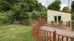 A small, single-story building with a wooden fence and a garden area. - Woods Edge (Mitcheldean)