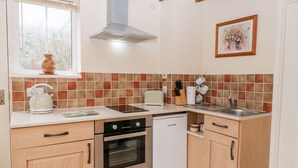 A compact kitchen with a built-in oven, a dishwasher, a window with a view, and a tiled backsplash. - Woods Edge (Mitcheldean)