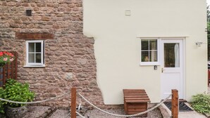 A stone building with a white door and windows, a small wooden bench, and a rope barrier. - Woods Edge (Mitcheldean)