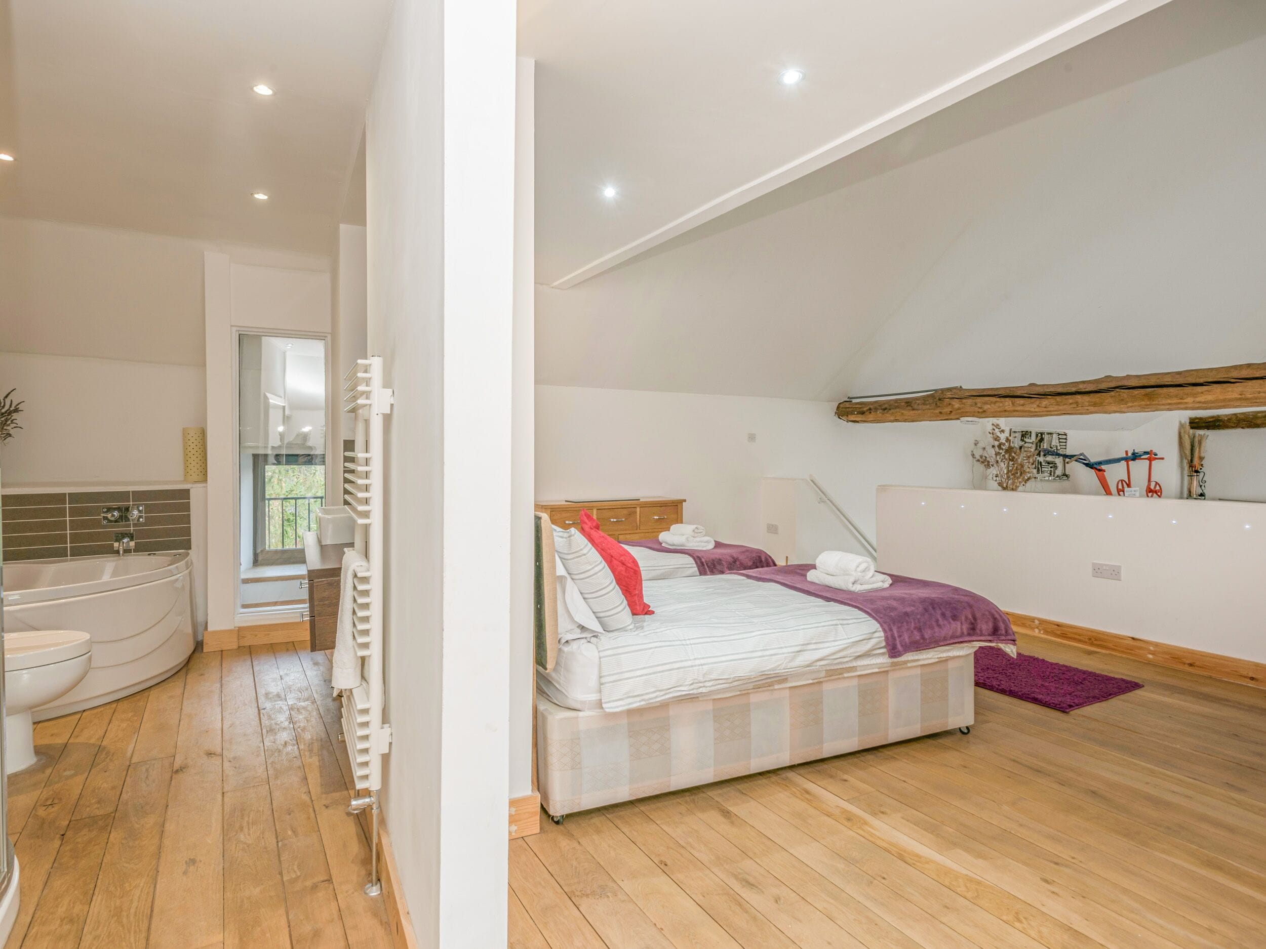 Un dormitorio moderno con una cama grande, una bañera integrada y suelo de madera.