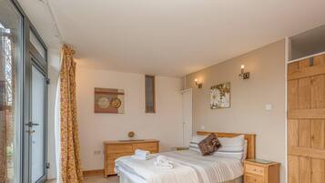 Een slaapkamer met een bed, houten nachtkastjes, een dressoir, een raam met gordijnen en een deur.