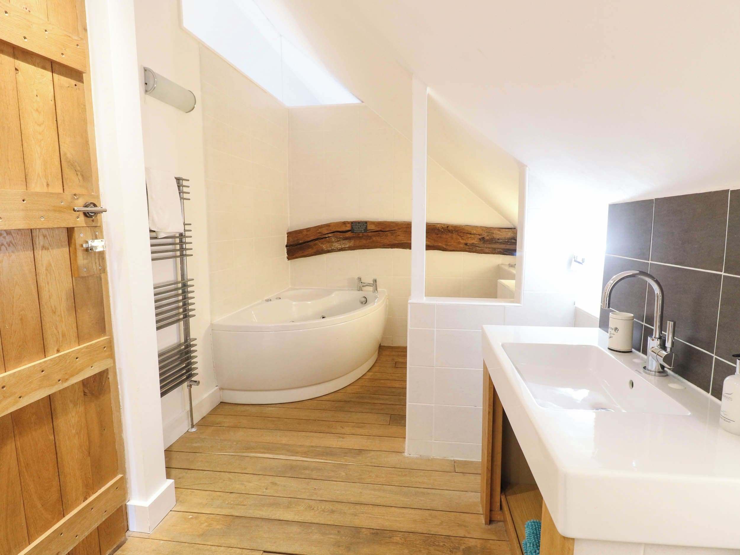A bathroom with a wooden door, a freestanding bathtub, a vanity with a sink, and a skylight.