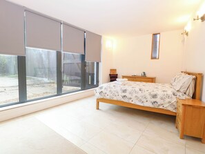 Une chambre à coucher avec un lit, des tables de chevet, un miroir et une fenêtre avec des stores.