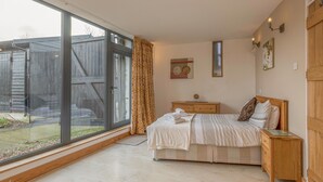 Une chambre avec une grande fenêtre, un lit, une table de chevet en bois et une petite table de nuit.