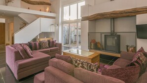 Un salon spacieux, doté d’un grand canapé, d’une cheminée et d’un escalier menant à l’étage supérieur.