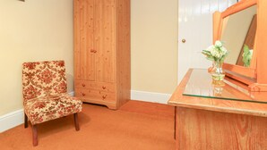 Une pièce comprenant une armoire en bois, un fauteuil à motifs floraux et une coiffeuse avec un miroir et un vase.