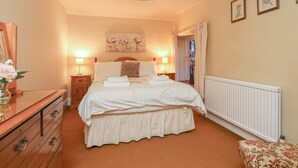 Une chambre à coucher comprenant un lit, des tables de chevet, une commode, un radiateur et des œuvres d’art encadrées accrochées au mur.
