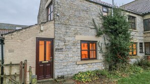 Une petite maison en pierre avec une porte et des fenêtres en bois, un petit jardin et une cheminée en briques.