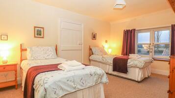 A bedroom with two beds, a window with curtains, and a door.