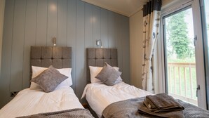 Ett hotellrum med två sängar, grå sänggavlar, vita sängkläder och utsikt över omgivningen genom ett fönster med gardiner.
