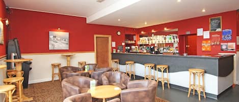 Eine Bar mit Ledersesseln, einer Theke voller Flaschen und einer roten Wand mit einer Uhr.