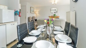 Un coin repas avec une table dressée pour quatre personnes, des chaises, un réfrigérateur, un canapé, un miroir et une horloge au mur.