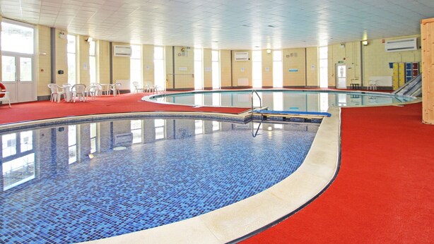 Une piscine intérieure avec un sol carrelé, entourée de fenêtres et de chaises.