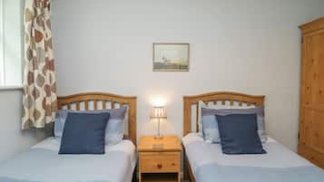 A twin bedroom with two beds, a nightstand, a lamp, a painting, and a wooden wardrobe.
