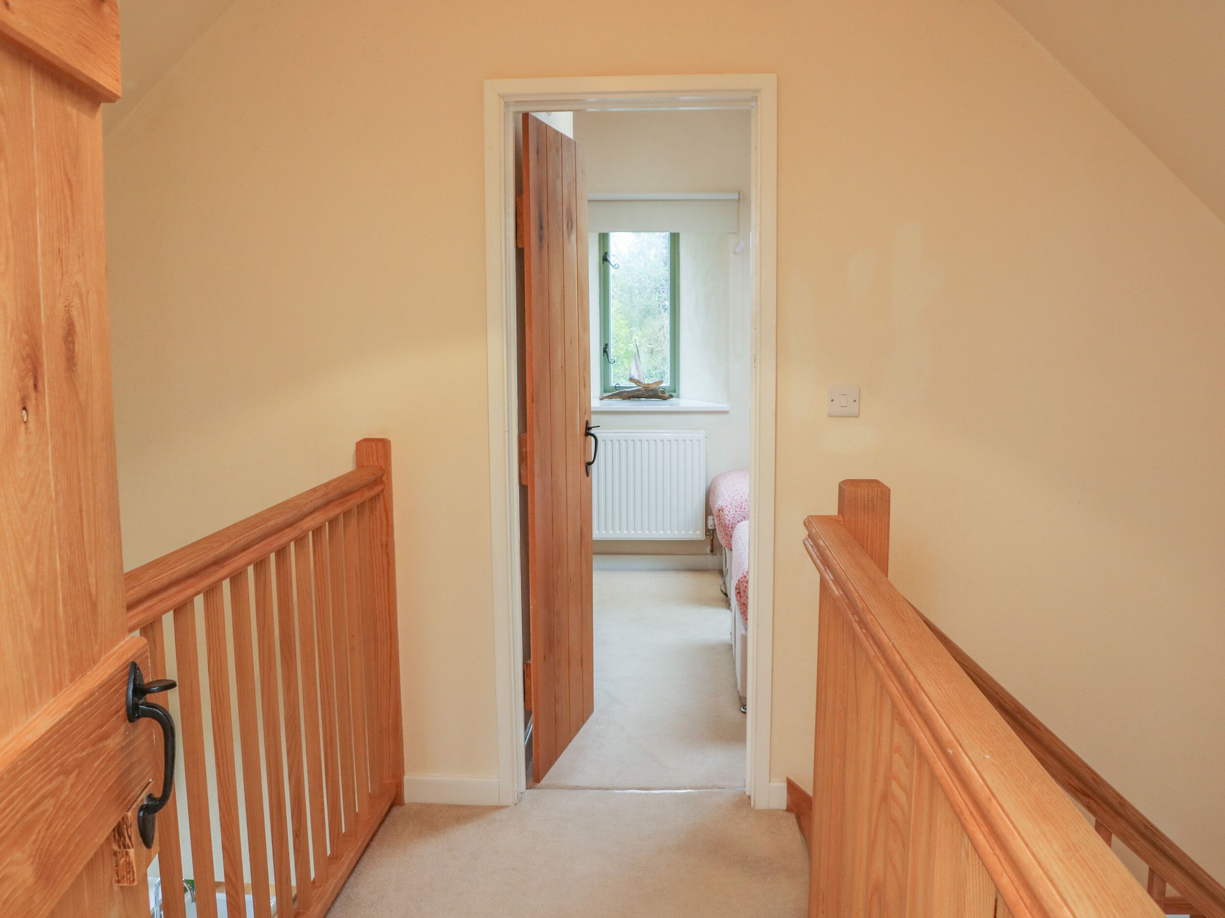 A narrow hallway with wooden railings leading to a bedroom with a window and radiator.