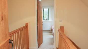 A narrow hallway with wooden railings leading to a bedroom with a window and radiator.