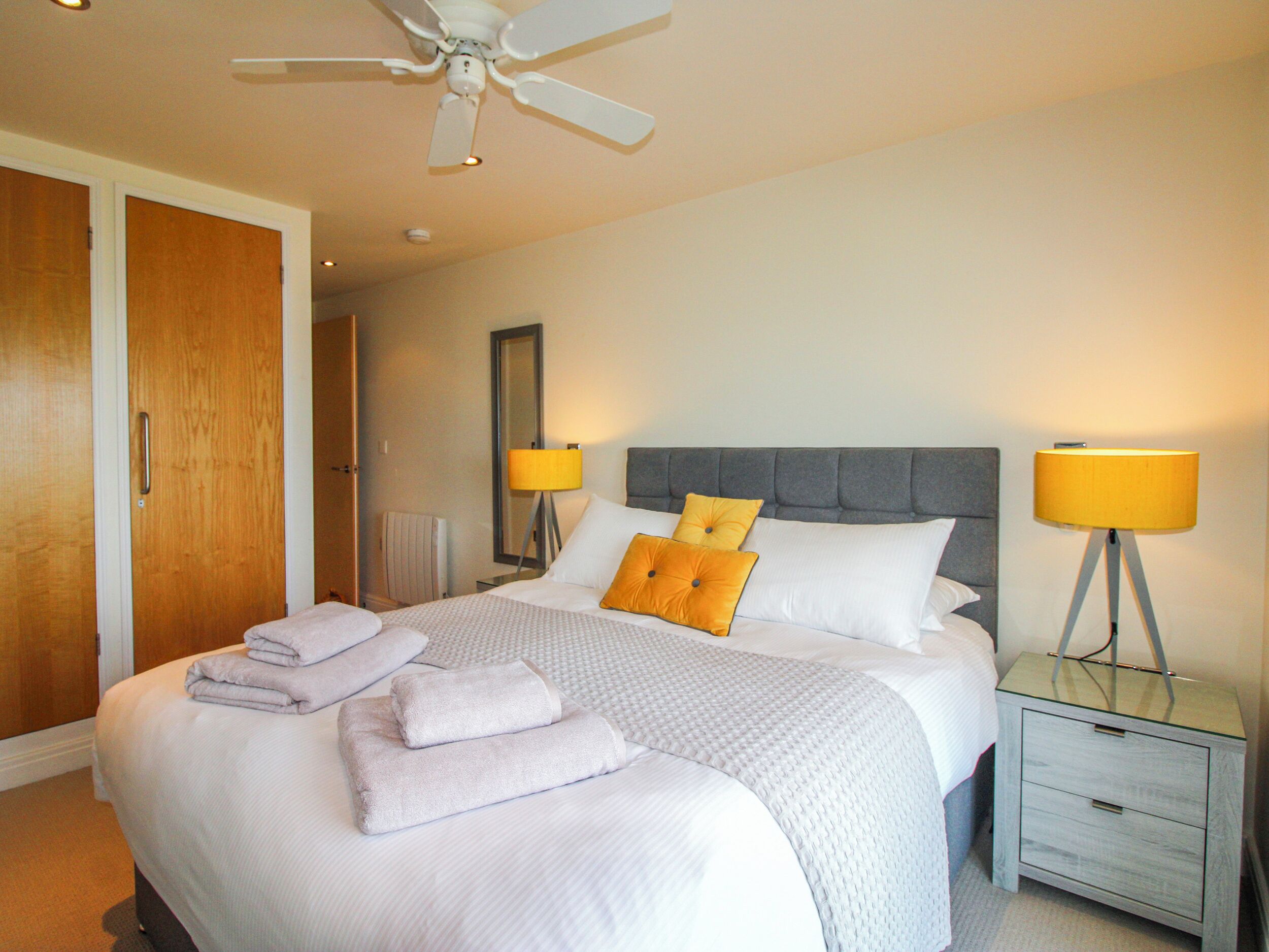 Habitación de hotel con cama, dos lámparas de noche, ventilador de techo y mesita de noche.