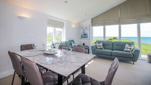 A dining area with a table set for six, a sofa, and a large window with a view of the sea. - 7 Ocean's Edge (Kingsbridge)