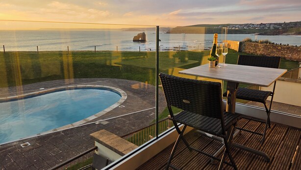 A balcony with a view of the sea, a pool, and a table with chairs. - 7 Ocean's Edge (Kingsbridge)