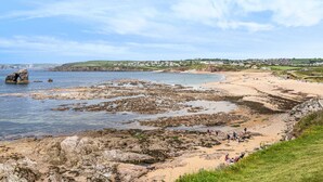 A coastal landscape with rocky shores, a sandy beach, and a village in the background. - 7 Ocean's Edge (Kingsbridge)