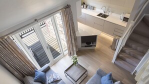 A modern living room with a grey sofa, a coffee table, and a view of a kitchen and balcony. - 4 Keeper's Cottage, Hillfield Village (Dartmouth)
