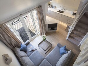 Un salon moderne avec un canapé gris, une table basse et une vue sur une cuisine et un balcon.