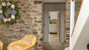 A stone-walled room with a yellow armchair, a dresser, and a doorway leading to another room. - Briar Barn (Bishop Auckland)