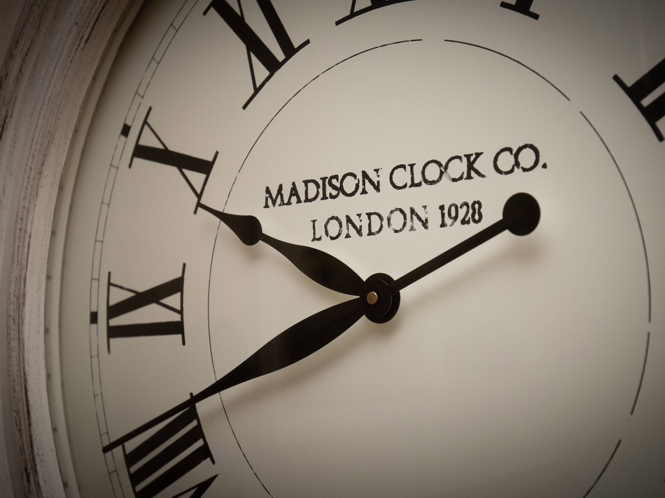 Un primer plano de la esfera de un reloj con números romanos y el texto "Madison Clock Co. London 1928".