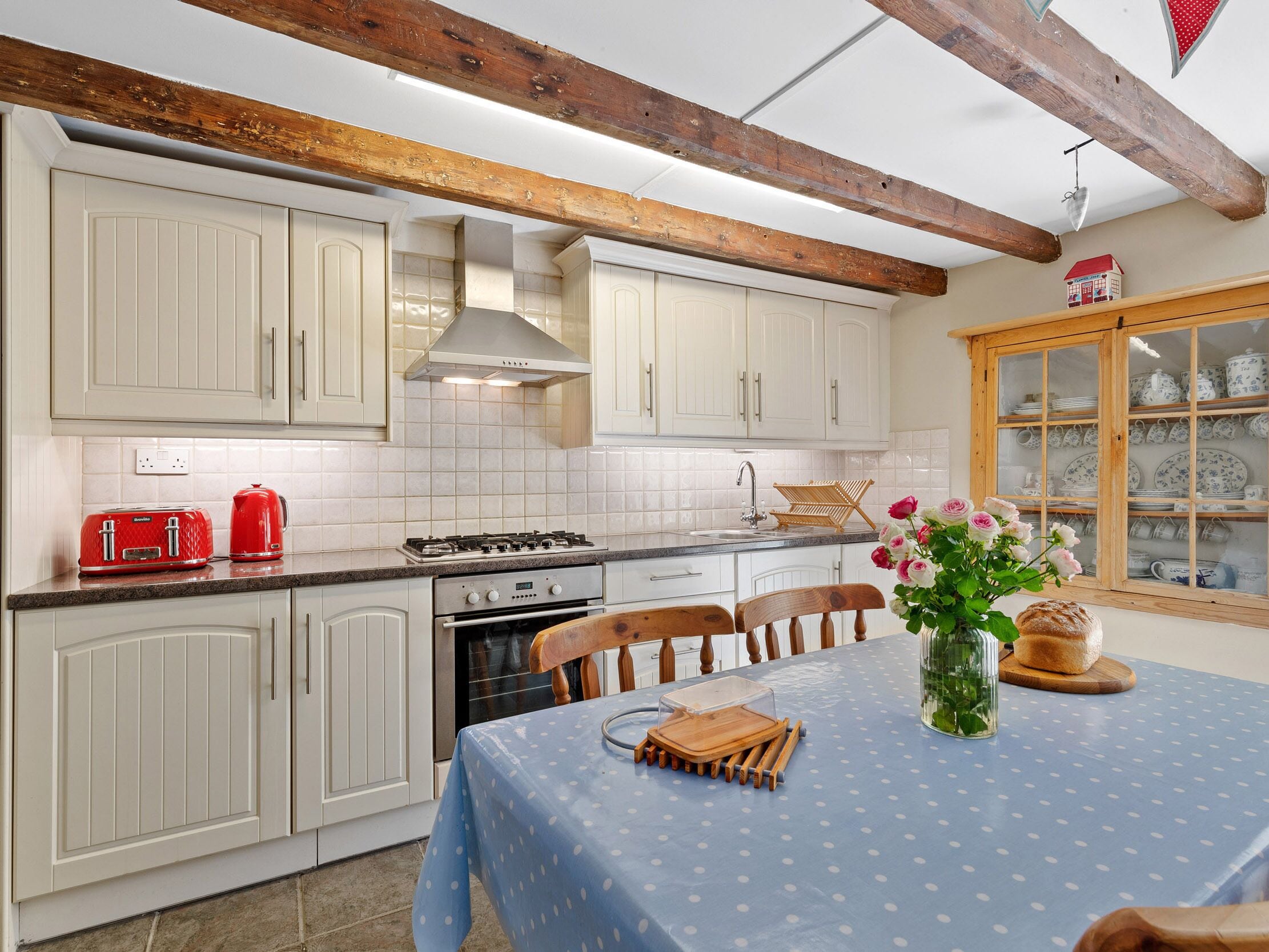 Een keuken met witte kastjes, een gasfornuis en een eettafel met een blauwe tafelkleed.