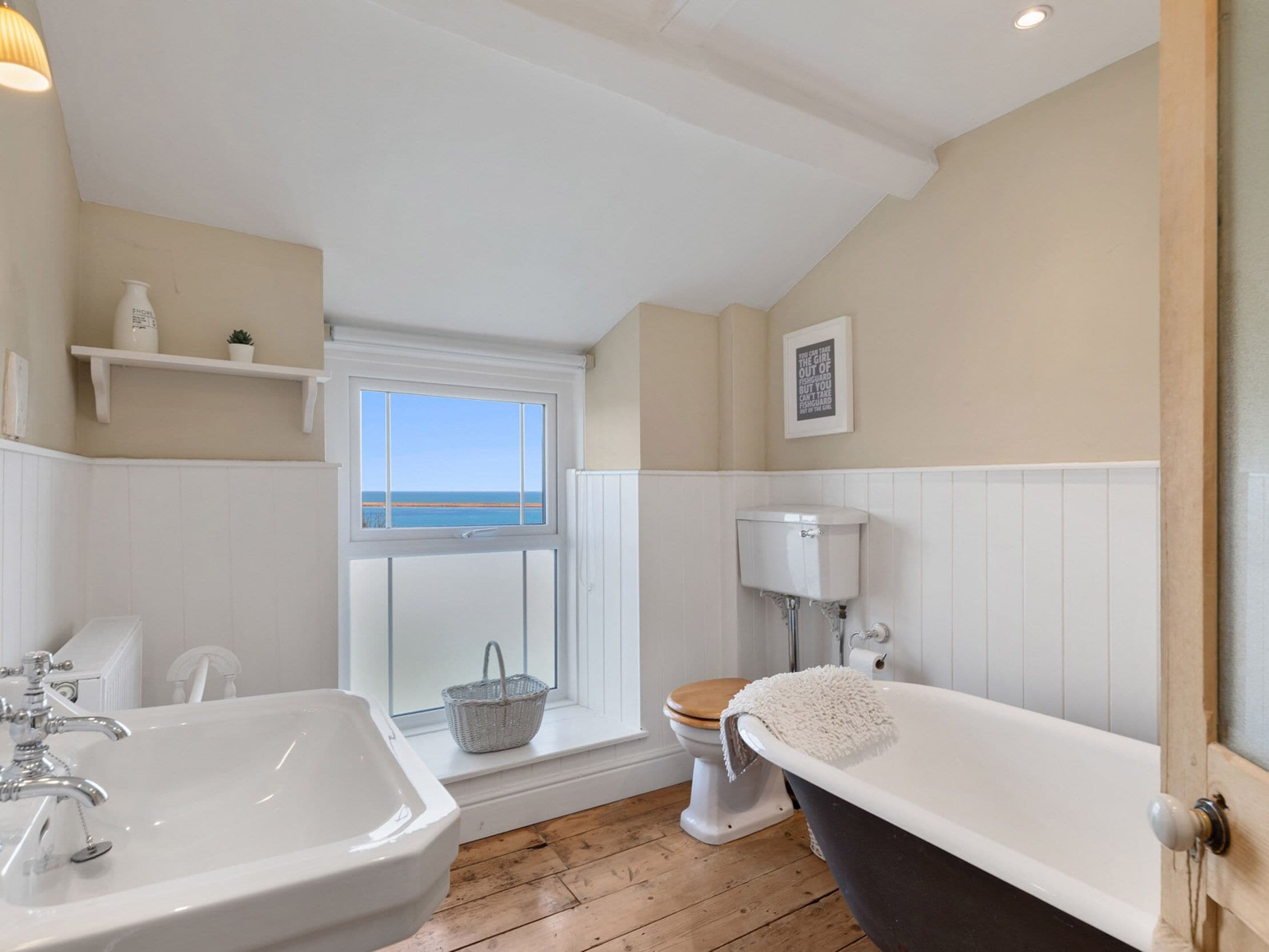 A bathroom with a large bathtub, a sink, a toilet, and a window with a view of the sea.