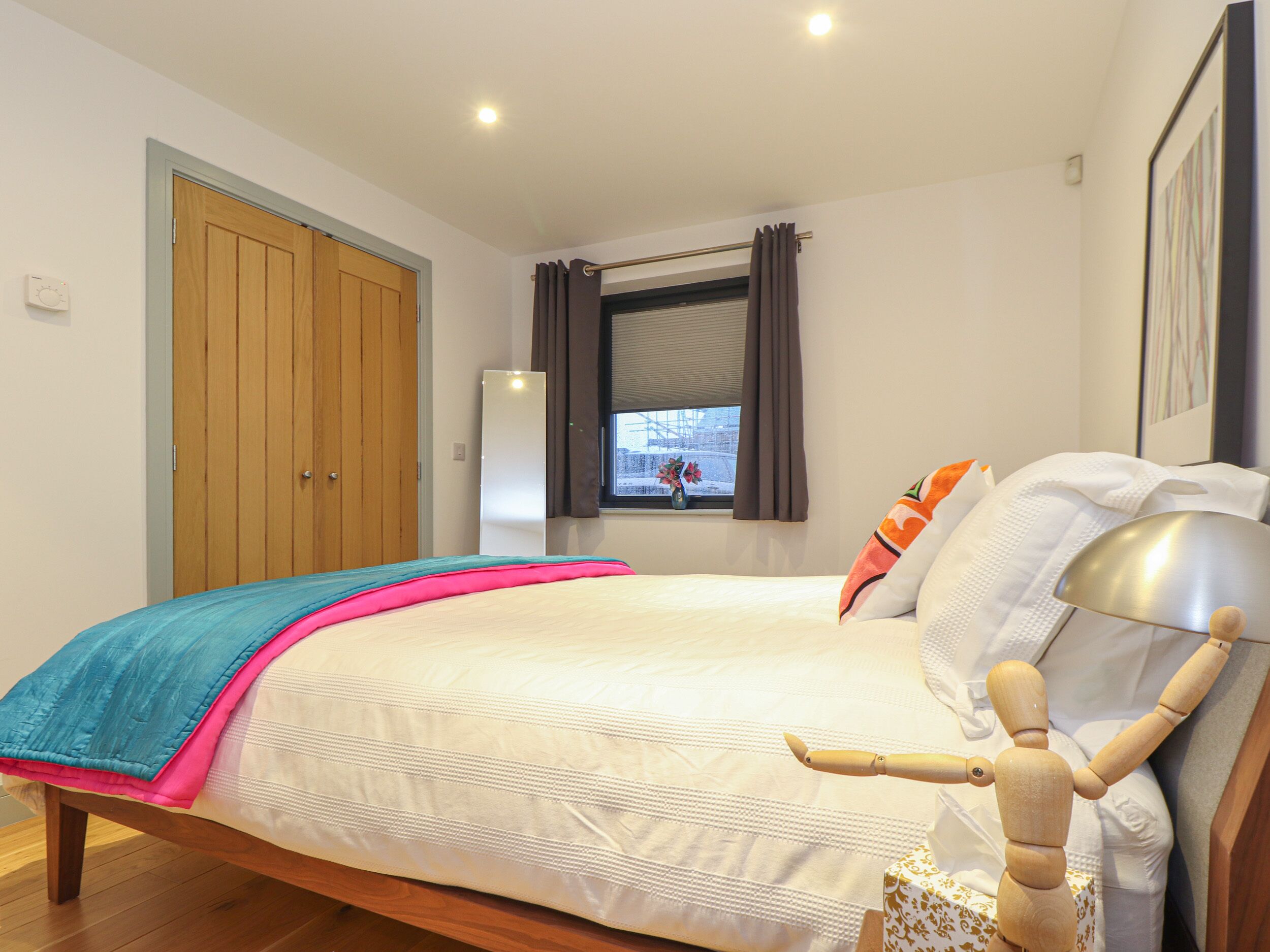 A bedroom with a bed, wooden wardrobe, window with curtains, and a bedside table with a lamp.