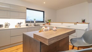 A modern kitchen with a wooden dining table, grey chairs, and a window providing natural light. - Idlewild, 2 Wheal Turnavore (St. Agnes)