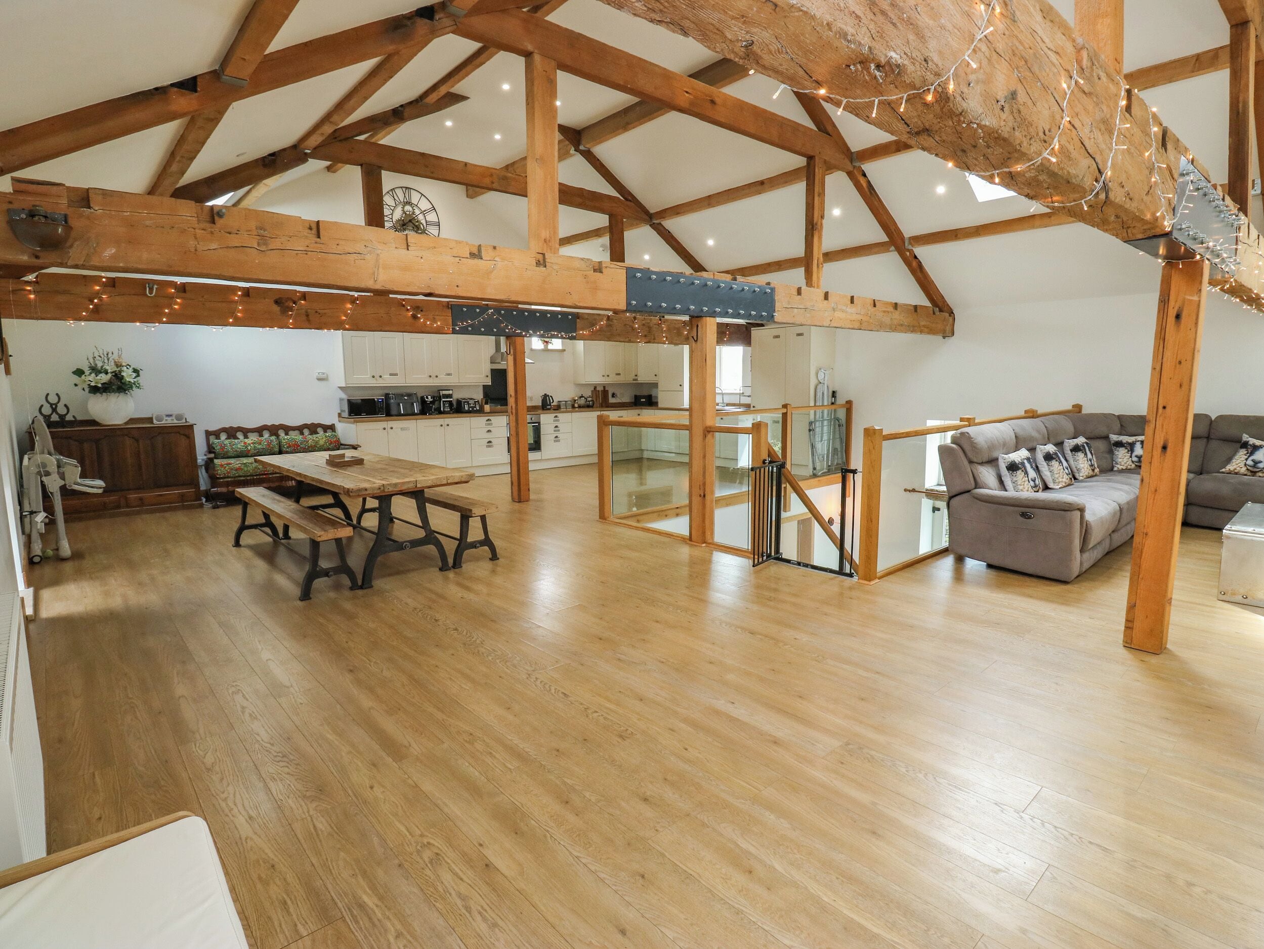 Un loft espacioso con vigas de madera expuestas, un comedor con mesa y bancos de madera, una cocina con armarios blancos y una sala de estar con sofá y cojines.